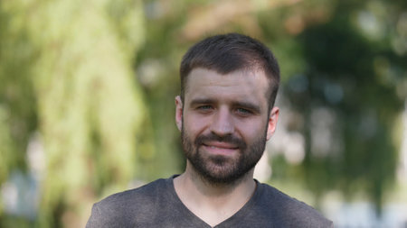 Man Smiles in a Casual Outdoor Setting During Daytime, Surrounded by Greenery and Natural Light, Showcasing a Relaxed Atmosphere and Friendly Demeanorの写真素材