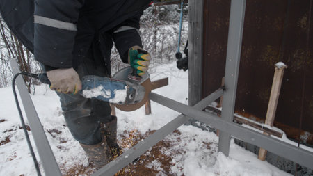 Worker Using an Angle Grinder on Metal Structure in Snowy Environment During Winter Construction Project Outdoorsの写真素材