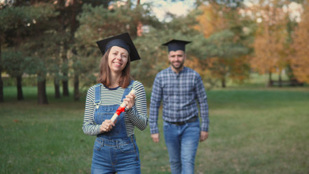 Graduates Celebrate Their Achievement Outdoors in a Park During Autumn, Showcasing Joy and Pride With a Diploma on a Sunny Dayの写真素材