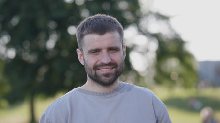 Smiling Man Outdoors During Daylight at a Park With Trees in the Background and a Relaxed Atmosphereの写真素材