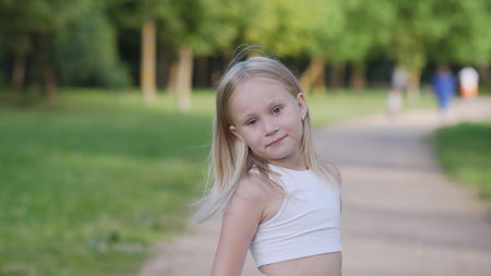 Young Girl in a White Shirt Poses Confidently on a Park Pathway Surrounded by Greenery on a Sunny Afternoonの写真素材