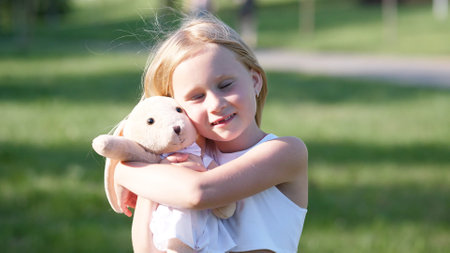 Young Child Enjoys Sunny Day Outside While Cuddling a Soft Toy on a Grassy Field During Afternoon Playtime in a Parkの写真素材