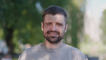 Smiling Man Outdoors in a Park During Daylight With Greenery in the Background, Exuding a Cheerful and Relaxed Vibeの写真素材