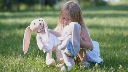 Young Child Plays With Plush Rabbits in a Sunny Green Field on a Warm Summer Afternoon, Enjoying the Simple Joys of Companionship and Imaginationの写真素材