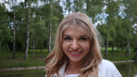 Smiling Woman Outdoors in Park With Lush Greenery and Trees, Enjoying a Sunny Day and the Beauty of Nature, Showcasing Happiness and Relaxationの写真素材