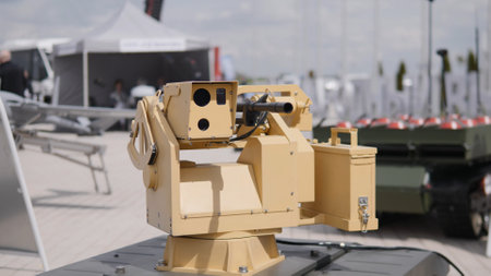 An unmanned ground vehicle outfitted with a precision weapon system is showcased at a defense technology exhibition, surrounded by military vehicles and equipment.の写真素材