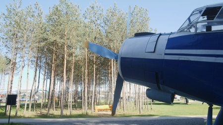 Vintage aircraft stands proudly with its distinctive propeller in a clear blue sky, surrounded by tall trees, offering a glimpse into aviation history and nature.の写真素材