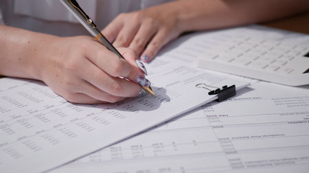 A person writing and organizing financial documents while using a calculator for analysis