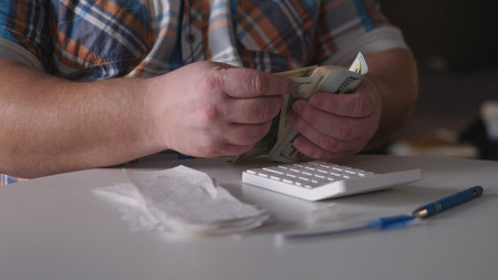 Counting cash in a dimly lit room with a calculator on the table during a late afternoon