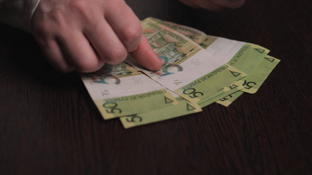 Hands Pointing At Polish Banknotes Spread On Table, Reflective Budgeting Scene With Notes Counted...