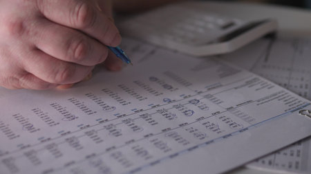Person writes notes on paper while using a calculator at a desk to manage financial information...