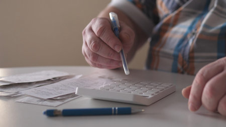 Person uses calculator to manage financial documents at a table with receipts and a pen during the...