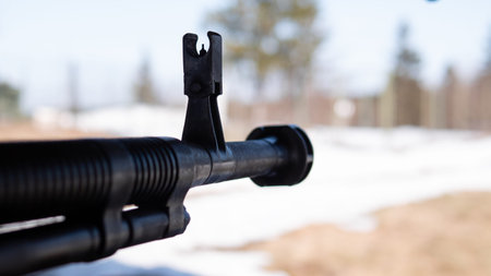 Close-up barrel and front sight of black rifle pointed outdoors over snowy field