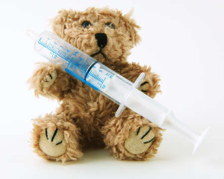 Teddy bear holding a syringe used to measure medication on a white backgroundの写真素材