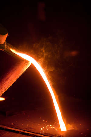Hot metal is poured from the bowl into a special form in a steel factory.の写真素材