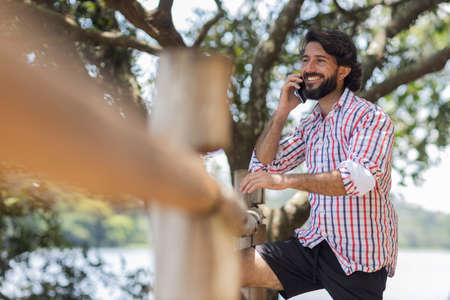 Young man at a park on a beautiful sunny day with mobile phone. Mobile phone for working and leisure. Home office concept. Green and nature background. high quality photoの写真素材