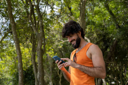 Young man at a park on a beautiful sunny day with mobile phone. Mobile phone for working and leisure. Home office concept. Green and nature background. high quality photoの写真素材