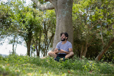 Young man at a park on a beautiful sunny day with mobile phone. Mobile phone for working and...