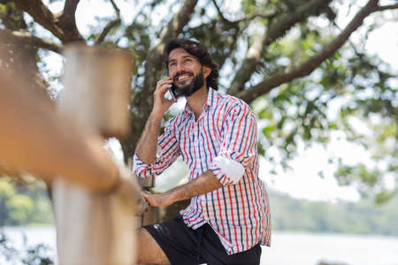 Young man at a park on a beautiful sunny day with mobile phone. Mobile phone for working and leisure. Home office concept. Green and nature background. high quality photoの写真素材