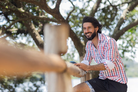 Young man at a park on a beautiful sunny day with mobile phone. Mobile phone for working and leisure. Home office concept. Green and nature background. high quality photoの写真素材