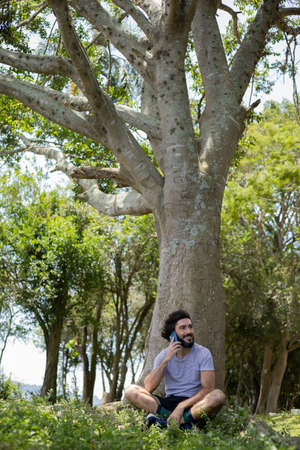 Young man at a park on a beautiful sunny day with mobile phone. Mobile phone for working and leisure. Home office concept. Green and nature background. high quality photoの写真素材