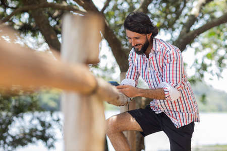 Young man at a park on a beautiful sunny day with mobile phone. Mobile phone for working and leisure. Home office concept. Green and nature background. high quality photoの写真素材