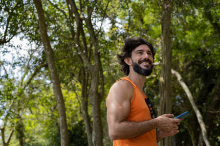Young man at a park on a beautiful sunny day with mobile phone. Mobile phone for working and leisure. Home office concept. Green and nature background. high quality photoの写真素材