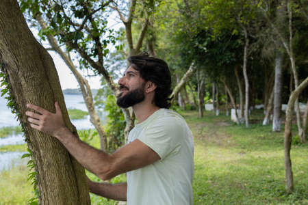 Portrait of smiling young man at a park on a beautiful sunny day. Man hugging a tree. Green and nature background. high quality photoの写真素材
