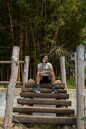 Young man at a park on a beautiful sunny day with mobile phone. Mobile phone for working and leisure. Home office concept. Green and nature background. high quality photoの写真素材