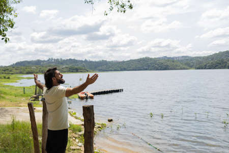 Portrait of smiling young man with open arms at a park on a beautiful sunny day. Green and nature background. Lagoon and lake, body of water. high quality photoの写真素材