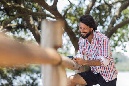 Young man at a park on a beautiful sunny day with mobile phone. Mobile phone for working and leisure. Home office concept. Green and nature background. high quality photoの写真素材