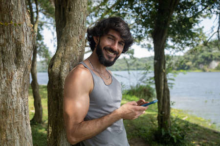 Young man at a park on a beautiful sunny day with mobile phone. Mobile phone for working and leisure. Home office concept. Green and nature background. high quality photoの写真素材