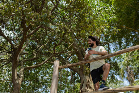 Young man at a park on a beautiful sunny day with mobile phone. Mobile phone for working and leisure. Home office concept. Green and nature background. high quality photoの写真素材