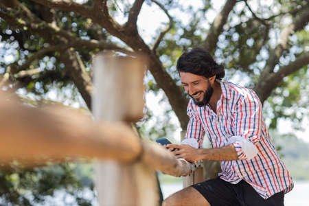 Young man at a park on a beautiful sunny day with laptop on his lap. Gray notebook for working and leisure. Home office concept. Green and nature background. high quality photoの写真素材