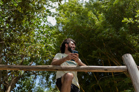 Young man at a park on a beautiful sunny day with laptop on his lap. Gray notebook for working and leisure. Home office concept. Green and nature background. high quality photoの写真素材