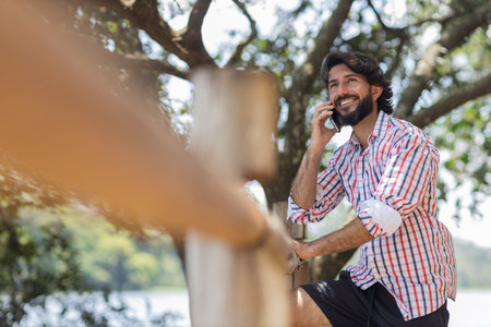 Young man at a park on a beautiful sunny day with mobile phone. Mobile phone for working and leisure. Home office concept. Green and nature background. high quality photoの写真素材
