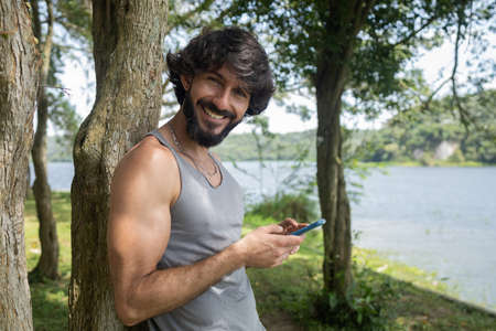 Young man at a park on a beautiful sunny day with mobile phone. Mobile phone for working and leisure. Home office concept. Green and nature background. high quality photoの写真素材