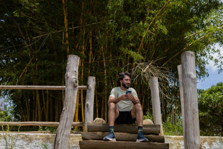 Young man at a park on a beautiful sunny day with mobile phone. Mobile phone for working and leisure. Home office concept. Green and nature background. high quality photoの写真素材