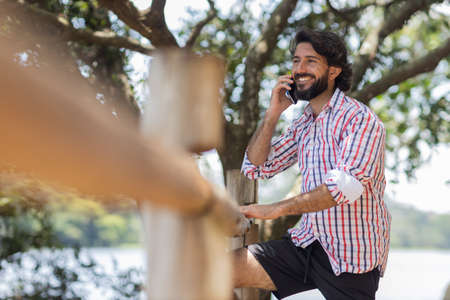 Young man at a park on a beautiful sunny day with mobile phone. Mobile phone for working and leisure. Home office concept. Green and nature background. high quality photoの写真素材