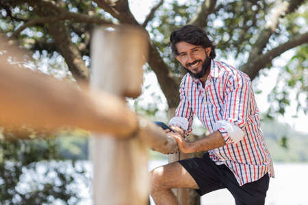 Young man at a park on a beautiful sunny day with mobile phone. Mobile phone for working and leisure. Home office concept. Green and nature background. high quality photoの写真素材