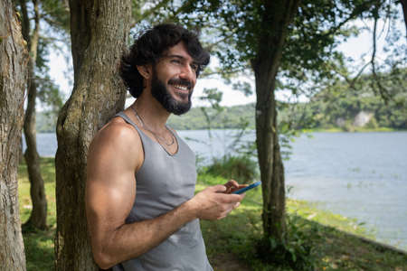Young man at a park on a beautiful sunny day with mobile phone. Mobile phone for working and leisure. Home office concept. Green and nature background. high quality photoの写真素材