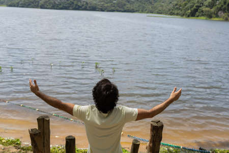 Portrait of smiling young man with open arms at a park on a beautiful sunny day. Green and nature background. Lagoon and lake, body of water. high quality photoの写真素材
