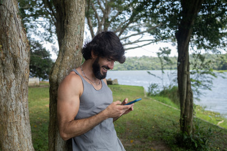 Young man at a park on a beautiful sunny day with mobile phone. Mobile phone for working and leisure. Home office concept. Green and nature background. high quality photoの写真素材