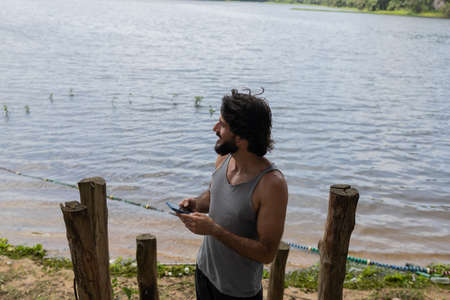 Young man at a park on a beautiful sunny day with mobile phone. Mobile phone for working and leisure. Home office concept. Green and nature background. high quality photoの写真素材