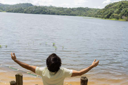 Portrait of smiling young man with open arms at a park on a beautiful sunny day. Green and nature background. Lagoon and lake, body of water. high quality photoの写真素材