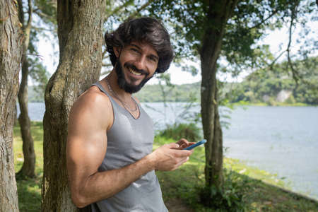 Young man at a park on a beautiful sunny day with mobile phone. Mobile phone for working and leisure. Home office concept. Green and nature background. high quality photoの写真素材