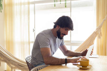 Young business man working at home in his kitchen with laptop and papers on kitchen wooden desk. Gray notebook for working. Home office concept. high quality photoの写真素材