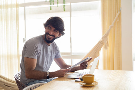 Young business man working at home in his kitchen with laptop and papers on kitchen wooden desk. Gray notebook for working. Home office concept. high quality photoの写真素材