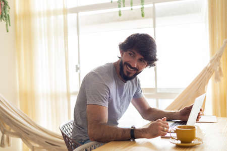 Young business man working at home in his kitchen with laptop and papers on kitchen wooden desk. Gray notebook for working. Home office concept. high quality photoの写真素材