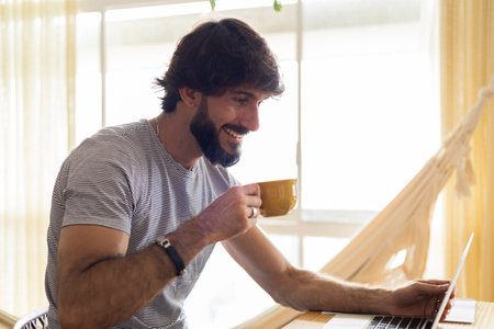 Young business man working at home in his kitchen with laptop and papers on kitchen wooden desk. Gray notebook for working. Home office concept. high quality photoの写真素材